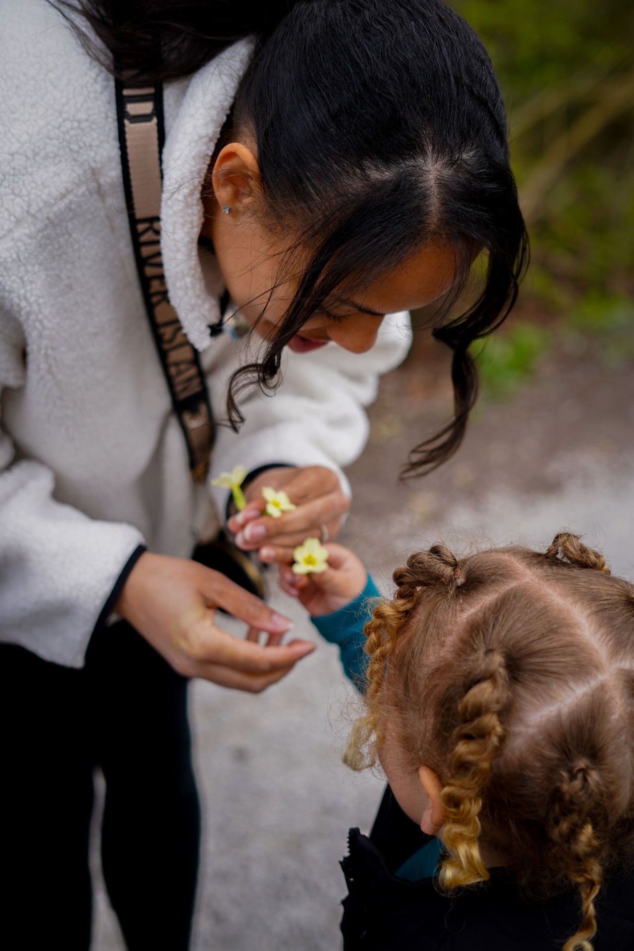Lottie leaning down with her child to look at a small flower together
