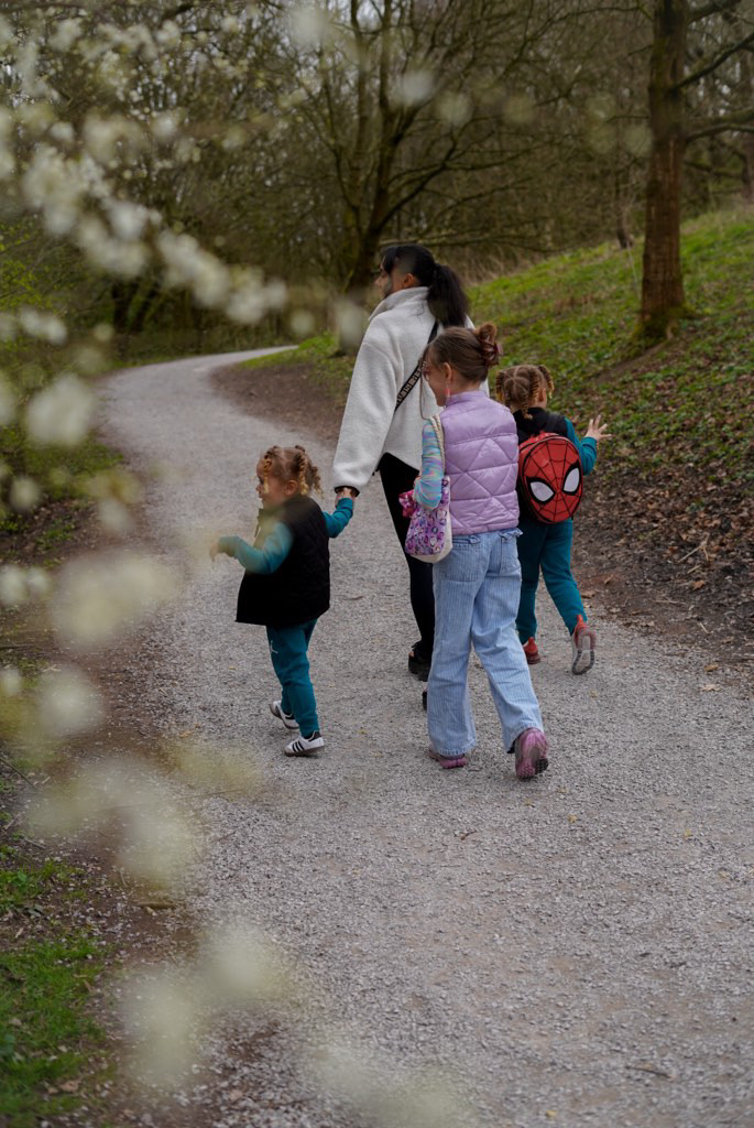 Lottie walking away along a woodland path, holding hands with her three children