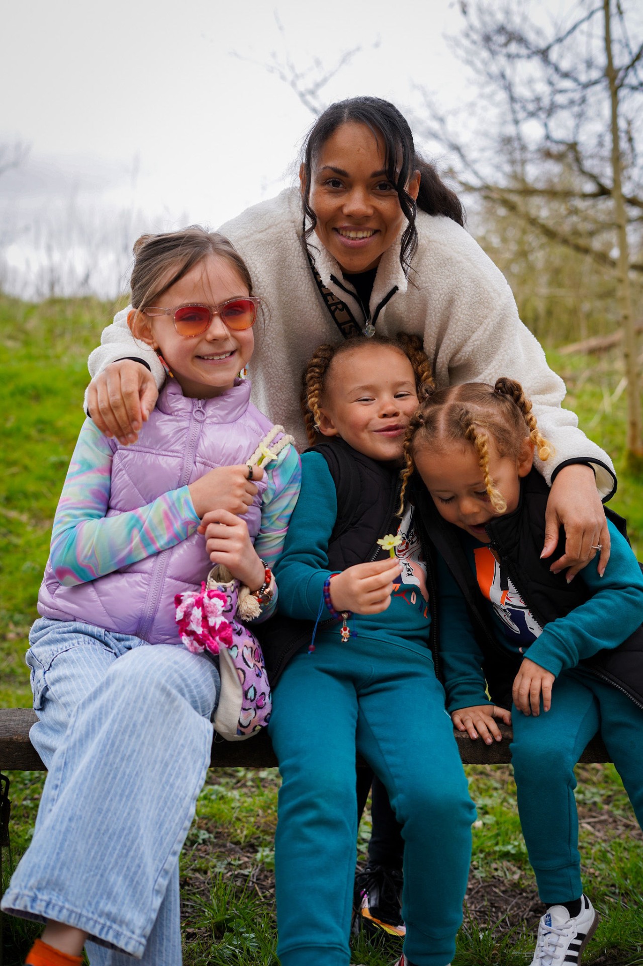 Lottie sitting on a wooden bench with her three children, all smiling together